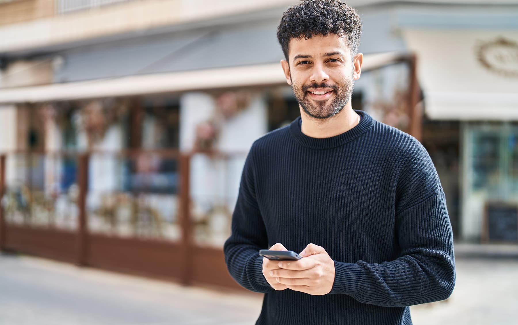 Mann mit Smartphone in der Hand lächelt in Kamera