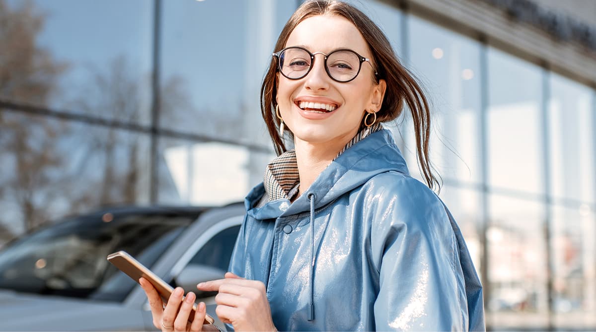 Dame mit Smartphone in der Hand lächelt in Kamera