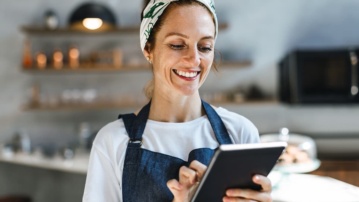 Frau in einem Cafè bedient ein Tablet und lächelt