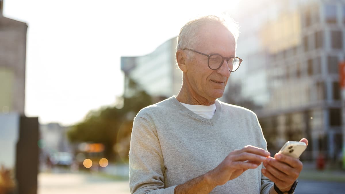 Älterer Mann ist in der Stadt und bedient Smartphone 